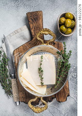 French hard goat cheese in a skillet with herbs. White background. Top view 98122276