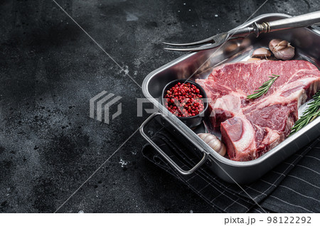 Fresh Raw porterhouse T bone beef meat Steak in steel tray with herbs. Black background. Top view. Copy space 98122292