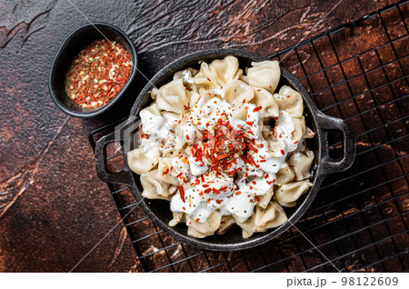 Cooking Manti Dumpling with yoghurt and tomato sauce in a skillet. Dark background. Top view 98122609