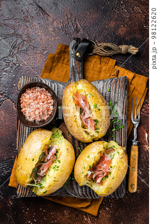 Jacket potatoes baked with cheese, herbs and butter. Dark background. Top view 98122620