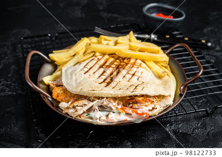 Doner kebab sandwich in grilled pita bread with vegetables and chicken meat. Black background. Top view Doner kebab sandwich in grilled pita bread with vegetables and chicken meat. Black background. Top view 98122733