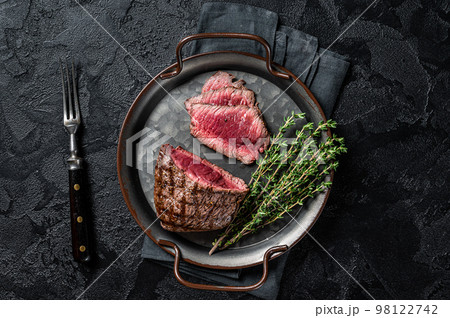 Grilled Rump sirloin steak sliced on a tray with herbs. Black background. Top view 98122742
