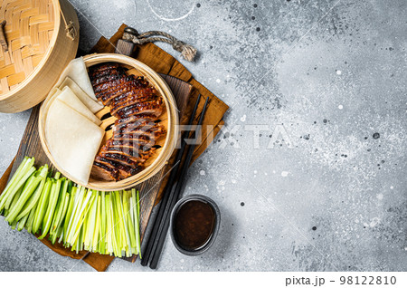 Peking Duck in bamboo steamer served with cucumber, green onion, and wheaten chinese pancakes and sauce Hoysin. Gray background. Top view. Copy space 98122810