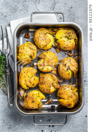 Broken potatoes baked with rosemary and thyme. Gray background. Top view Broken potatoes baked with rosemary and thyme. Gray background. Top view 98122979