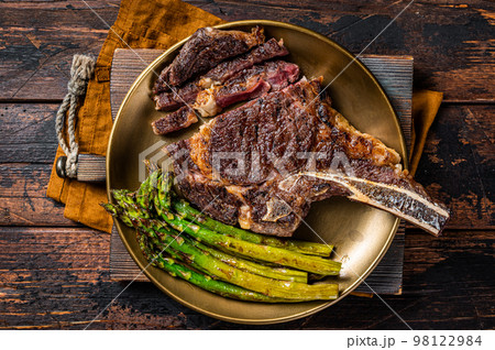 Sliced Grilled Cowboy or rib eye with bone beef steak, roasted asparagus in a plate. Wooden background. Top view 98122984