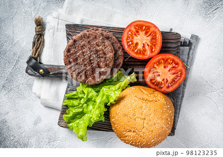 Fried cutlet for burger with vegetables and spices on wooden board. White background. Top view Fried cutlet for burger with vegetables and spices on wooden board. White background. Top view 98123235