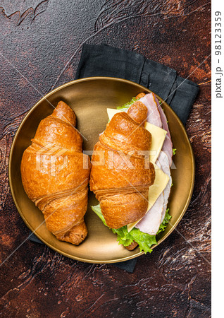 French croissant sandwich with lettuce, cheese, tomatoes and ham. Dark background. Top view French croissant sandwich with lettuce, cheese, tomatoes and ham. Dark background. Top view 98123359
