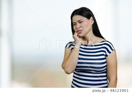 Woman suffering from toothache touching her cheek. Bright windows background. Woman suffering from toothache touching her cheek. Bright windows background. 98123901