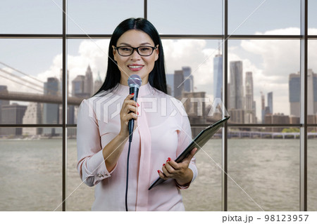 Portrait of business woman with a microphone and clipboard. Checkered windows and cityscape background. 98123957
