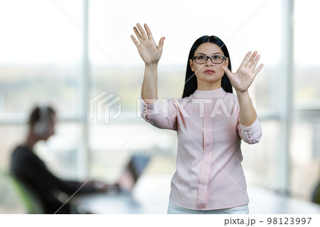 Young asian woman is zooming in objects on imaginary virtual screen for copy space. Office enviroment background. Young asian woman is zooming in objects on imaginary virtual screen for copy space. Office enviroment background. 98123997