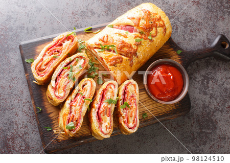 Delicious pizza stromboli roll stuffed with salami sausage and mozzarella cheese close-up on a wooden board. horizontal top view 98124510
