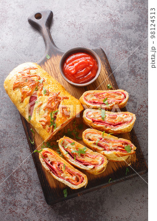 Homemade Stromboli pizza with cheese, pepperoni, salami closeup on the wooden board. Vertical top view 98124513