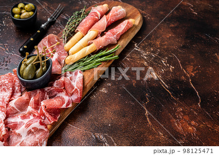 Meat appetizer platter with grissini sticks, Prosciutto crudo, Salami and Coppa Sausage and olives. Dark background. Top view. Copy space 98125471