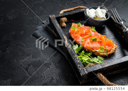 Sandwich with salmon fillet and cream cheese in wooden tray. Black background. Top view. Copy space 98125554