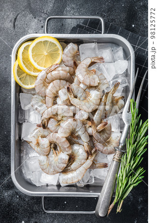 Raw pacific white shrimp prawn peeled with tail on ice. Black background. Top view Raw pacific white shrimp prawn peeled with tail on ice. Black background. Top view 98125772