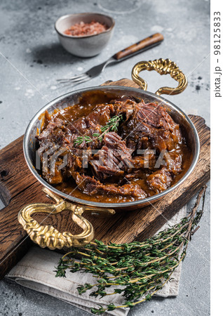 German braised beef cheeks in brown red wine sauce. Gray background. Top view German braised beef cheeks in brown red wine sauce. Gray background. Top view 98125833