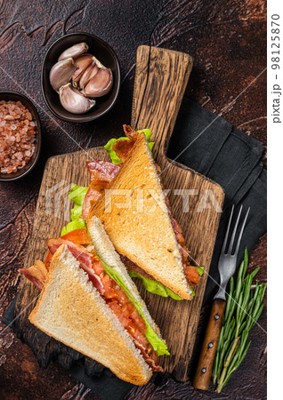 Classic BLT sandwich with bacon, tomato and lettuce on wooden board with herbs. Dark background. Top view 98125870