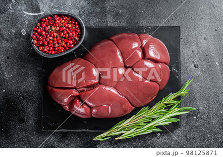 Beef veal kidney, raw offal meat on marble board with rosemary. Black background. Top view 98125871