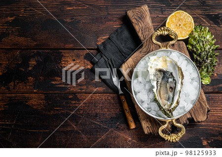 Appetizing raw oyster with ice cubes in a skillet . Wooden background. Top view. Copy space Appetizing raw oyster with ice cubes in a skillet . Wooden background. Top view. Copy space 98125933