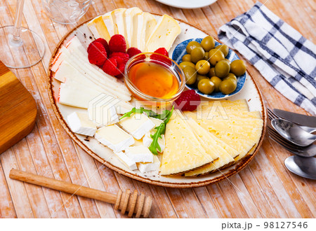 Cheese plate served with honey and raspberries on wooden table Cheese plate served with honey and raspberries on wooden table 98127546
