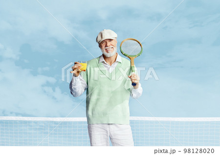Portrait of handsome senior man in stylish white outfit posing with tennis racket and fresh juice over sky blue background. Concept of leisure activity, hobby, lifestyle 98128020