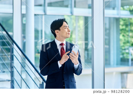 オフィスでスマホを操作するスーツ姿のビジネスマン オフィスでスマホを操作するスーツ姿のビジネスマン 98128200