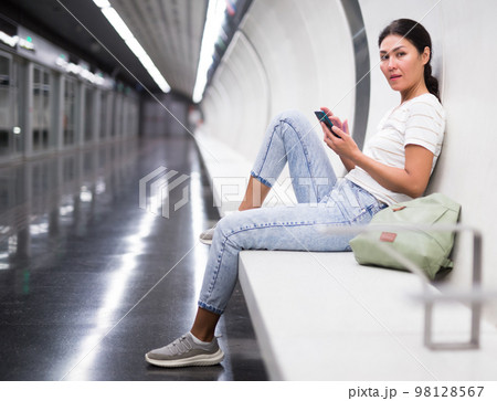 Woman with smartphone sitting on bench in subway station Woman with smartphone sitting on bench in subway station 98128567