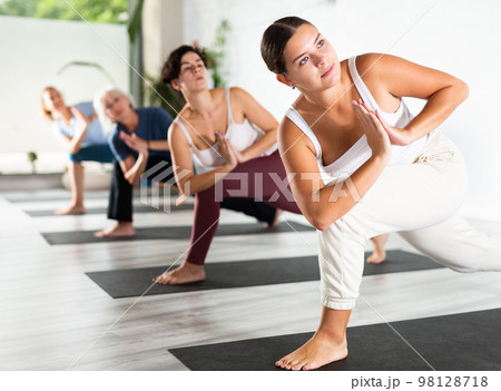 Calm young woman practicing Revolved Side Angle Pose Parivrtta Parsvakonasana, balancing posture of Hatha yoga during group workout in studio Calm young woman practicing Revolved Side Angle Pose Parivrtta Parsvakonasana, balancing posture of Hatha yoga during group workout in studio 98128718