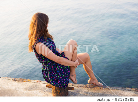 The girl in a beautiful dress is sitting on the pier. The girl in a beautiful dress is sitting on the pier. 98130889