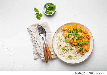 Traditional Indian dish chicken curry with basmati rice and fresh cilantro on rustic white plate on white concrete table background from above. Indian dinner meal Traditional Indian dish chicken curry with basmati rice and fresh cilantro on rustic white plate on white concrete table background from above. Indian dinner meal 98132775
