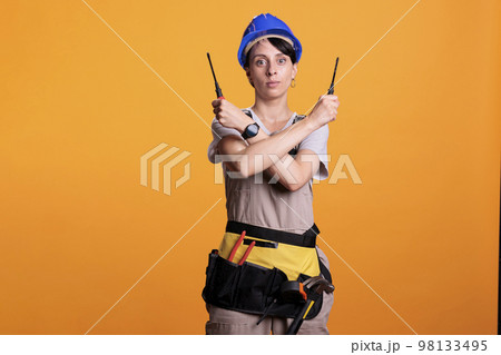 Woman construction worker holding screwdrivers with both hands looking at camera in studio. Female building contractor doing stop sign and expressing refusal or rejection, x shape. 98133495