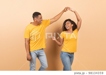 Cheerful african american couple dancing over yellow background, happy romantic black spouses having fun together Cheerful african american couple dancing over yellow background, happy romantic black spouses having fun together 98134359