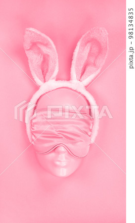 Pink sleeping eye mask on mannequin face with fluffy Easter bunny ears. Image is toned in Viva Magenta color of year 2023. sleeping disorder. Holidays, Head accessory. Plastic face. 98134835