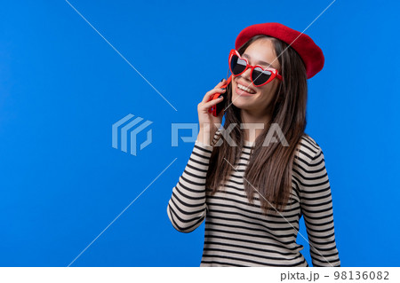 Stylish french woman talking by phone, nice joke, smiling. Young lady on blue background. Having 98136082