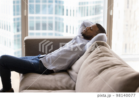 Calm African man put hands behind head resting on sofa Calm African man put hands behind head resting on sofa 98140077