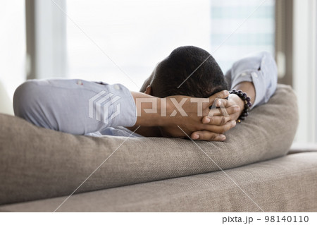 Unknown African single man relaxing leaned on sofa, closeup Unknown African single man relaxing leaned on sofa, closeup 98140110