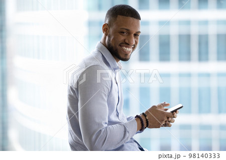 African businessman holds smartphone smile pose in modern office building 98140333