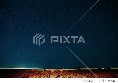 Agricultural Colorful Background Copy Space. Night Starry Sky Above Rural Landscape Field Meadow With Rolls Of Straw In Fields After Harvest. Glowing Stars And Sunset Lights Hay Bales After Harvest 98140336
