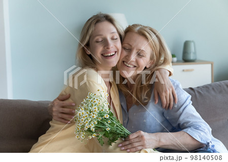 Happy peaceful young adult daughter girl giving flowers to mom, 98140508