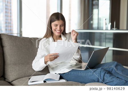 Excited woman sits on sofa read paper notice feels happy Excited woman sits on sofa read paper notice feels happy 98140629