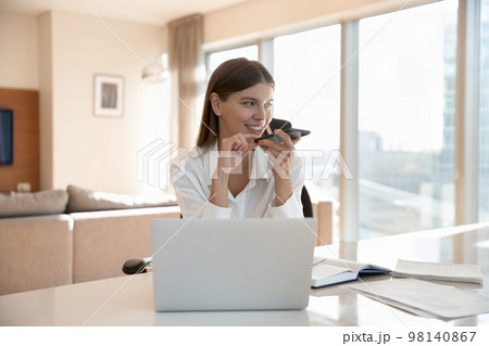 Woman having call on speakerphone seated at workplace desk Woman having call on speakerphone seated at workplace desk 98140867