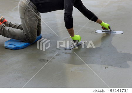 As he holds steel masonry trowel in his hand masonry worker smooths plastering concrete to cement floor As he holds steel masonry trowel in his hand masonry worker smooths plastering concrete to cement floor 98141754