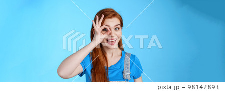 Cheerful upbeat redhead european female feel lucky inspired, look through circle okay on eye, smiling broadly amused, look wondered admire cool awesome sales, stand blue background Cheerful upbeat redhead european female feel lucky inspired, look through circle okay on eye, smiling broadly amused, look wondered admire cool awesome sales, stand blue background 98142893