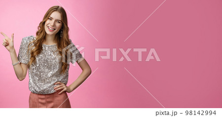 Portrait attractive caucasian woman attend glamour party dressed glittering blouse, pointing upper left corner discuss product smiling satisfied happily, casual pose conversation pink background 98142994