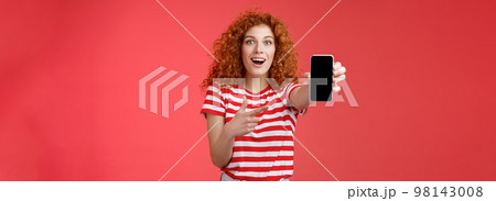 Take look what awesome smartphone. Impressed excited good-looking female love digital innovations redhead girl curly hairstyle showing phone screen pointing display promote cool app 98143008