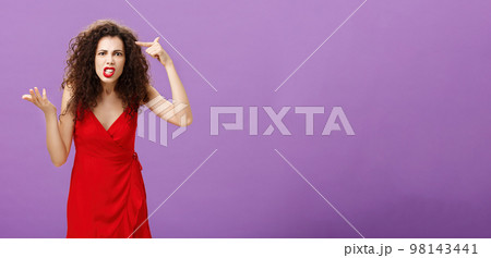 Outraged and pissed wife critisize dumb idea, outraged and fed up with stupid husband actions rolling finger near temple gesturing with raised palm, being angry and questioned over purple background Outraged and pissed wife critisize dumb idea, outraged and fed up with stupid husband actions rolling finger near temple gesturing with raised palm, being angry and questioned over purple background 98143441