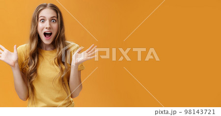 Impressed excited girl describing feelings sharing positive impression gesturing with palms during talk open mouth from amazement and oy communicating lively over orange background Impressed excited girl describing feelings sharing positive impression gesturing with palms during talk open mouth from amazement and oy communicating lively over orange background 98143721