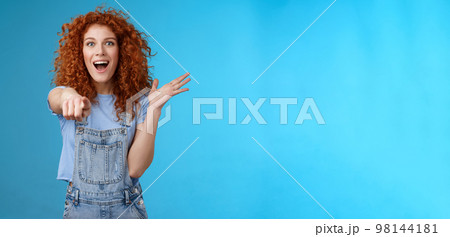 Excited impressed surprised cute redhead european woman curly astonished happily pointing index finger camera gesturing lively thrilled see awesome thing reacting amazed standing blue background Excited impressed surprised cute redhead european woman curly astonished happily pointing index finger camera gesturing lively thrilled see awesome thing reacting amazed standing blue background 98144181