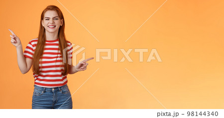 Carefree happy redhead female celebrating good news, feel happy joyful, smiling toothy white grin, enjoy sunny summer day going beach, dancing from rejoice and positive emotions, pointing left right 98144340