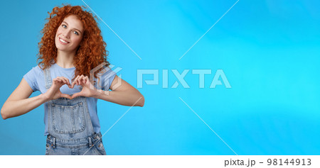 Caring tender lovely redhead girlfriend express sympathy tenderness gentle sympathy tilt head smiling broadly show heart love gesture chest cherish passionate romantic feelings, blue background 98144913